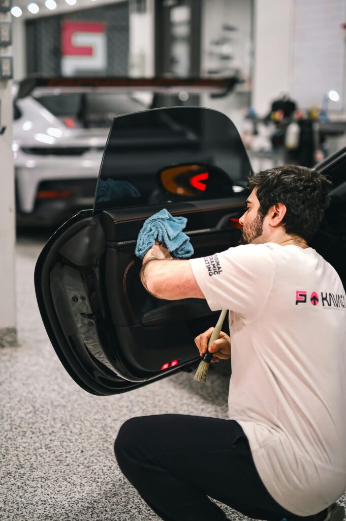A man meticulously cleans a car door at an auto shop, emphasizing detailing and service.