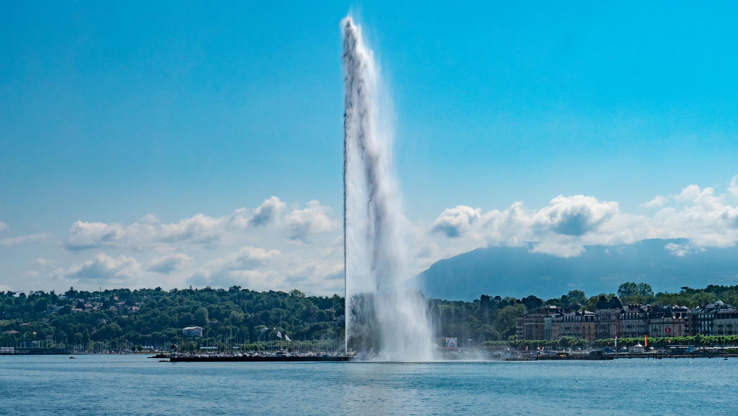 Breathtaking view of Geneva's Jet d'Eau fountain against blue sky and mountain backdrop.