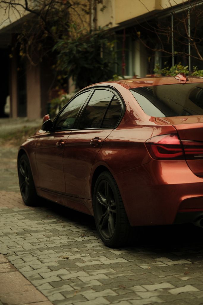 A sleek red car parked on a cobblestone street surrounded by urban greenery.