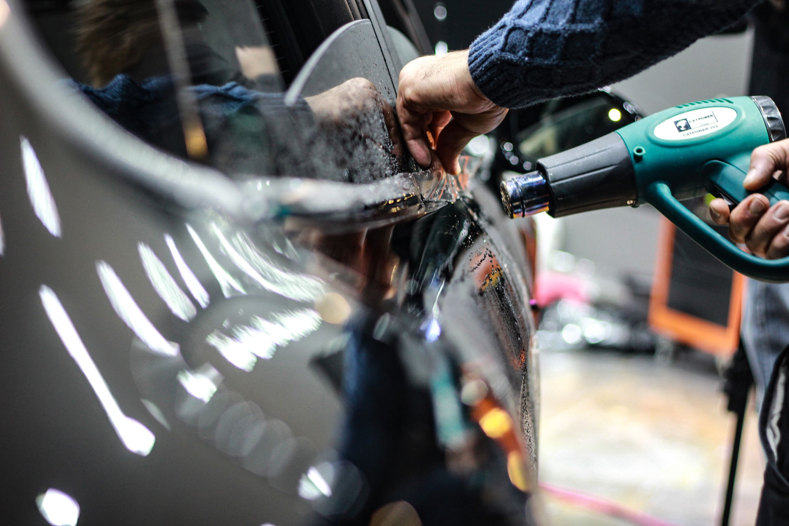 Close-up of a worker using a heat gun for car detailing in an indoor garage setting.