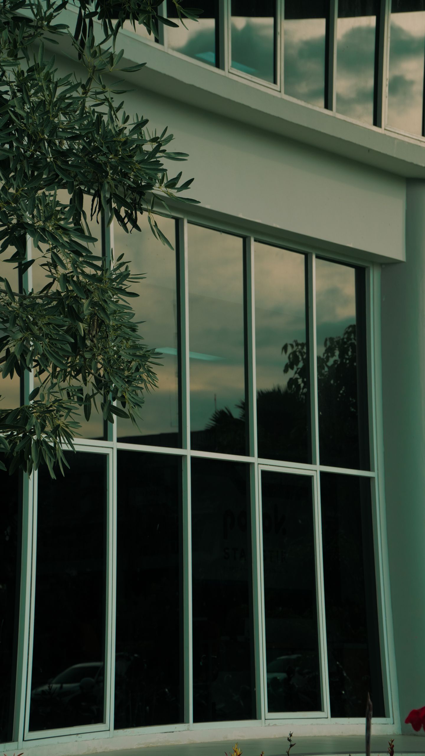 View of a modern building with reflective windows and nearby foliage against a cloudy sky.